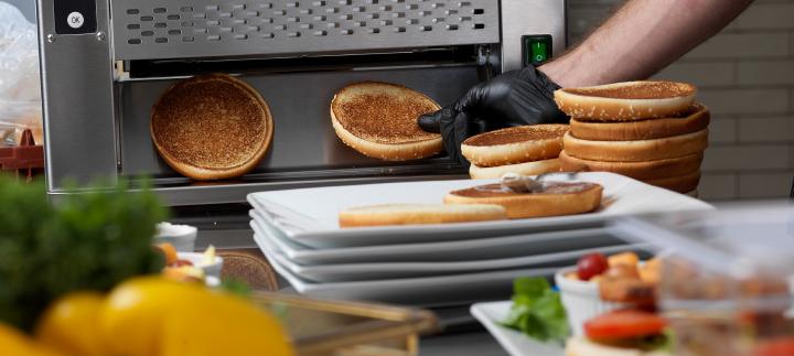a gloved hand removes hamburger buns from a toasting machine